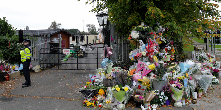 14/10/2015 Flowers lay outside the Carrickmines halting site where a fire claimed the lives of 10 people, including five children, as residents of Rockville Drive block access to a site earmarked for the survivors, accommodating the 15 adults and children until a permanent dwelling is ready. The Rockville Road residents wait for news from the meeting of officials from Dun Laoghaire-Rathdown County Council and residents living near a site earmarked for survivors of the Carrickmines fire as a large digger sits parked down the road. Photo: RollingNews.ie