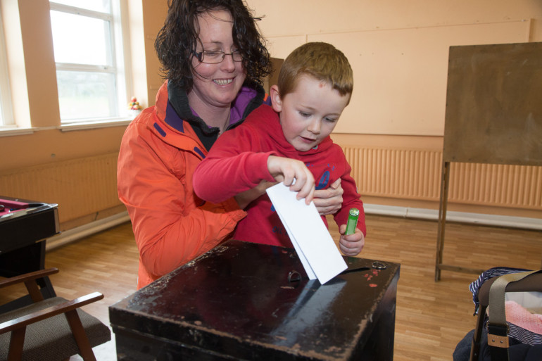 Liam O'Sullivan, (5) Cill Rónáin, Aran Islands is watched by his mother, Yvonne, as he casts her vote in the island polling station at Scoil Rónáin NS, Inis Mór. Pic: Seán Ó Mainnín.